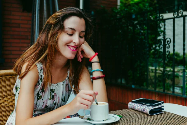 Stock photo taken of a smiling woman sitting on the terrace of a cafe drinking coffee with milk