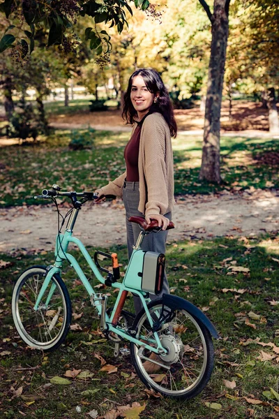 Stock photo taken of a smiling woman riding her bike through a park enjoying an autumn day