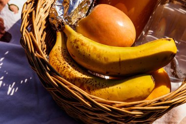 Güneşli bir sonbahar gününde muz, elma suyu ve elmadan oluşan meyve pikniği sepeti.