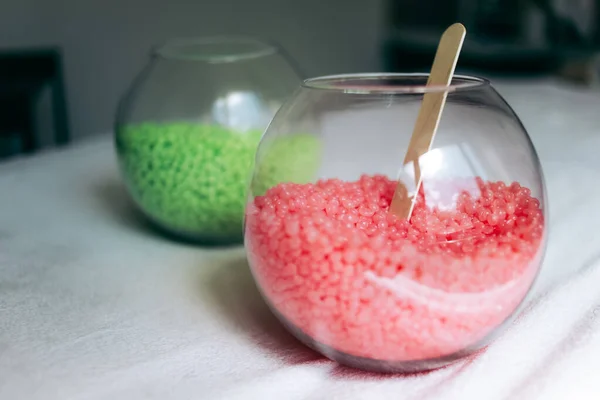 İki yuvarlak cam vazo, pembe ve yeşil balmumu granüller ve beyaz arka planda tahta sopa..