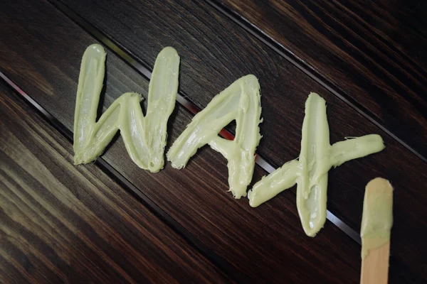 Top view on inscription wax laid out with hot wax for depilation and spatula with wax near it on wooden background. The concept of depilation, epilation, waxing, shugaring.
