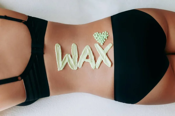 Top view on inscription wax laid out with hot wax for depilation. Heart which composed of granules of depilatory wax. Hair removal procedure on female back. The concept of epilation, waxing, shugaring