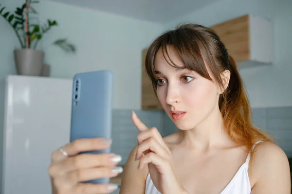 Young pretty girl with the bangs reading a message or shopping online in a smartphone at home in blue interior