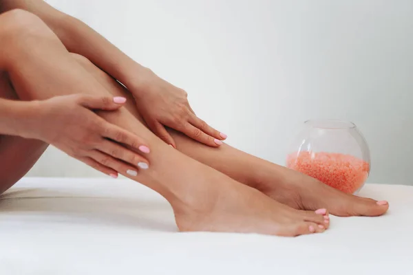 Uzun kadın bacakları, arka planda epilasyon işleminden sonra. Ayaklarını okşayan bir kız. Epilasyon, ağda, titreme, cilt bakımı, manikür ve pedikür konsepti.