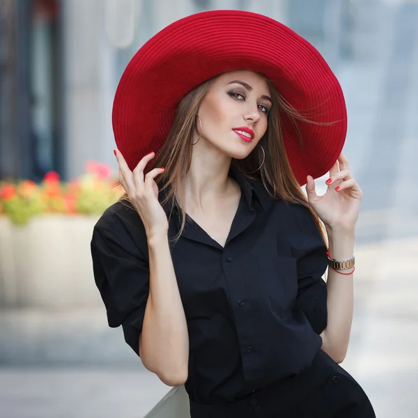 Schöne junge modische Frau posiert in schwarzem Kleid und rotem Hut. Modestil. — Stockfoto