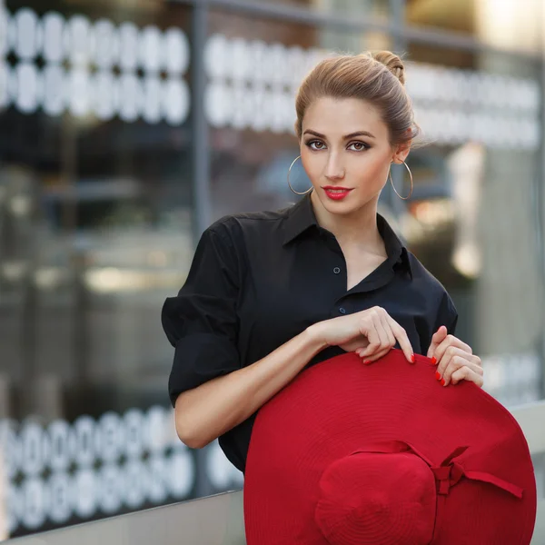 Schöne junge modische Frau posiert in schwarzem Kleid und rotem Hut. Modestil. — Stockfoto