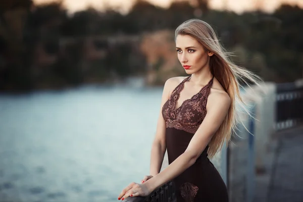 Mulher na moda jovem bonita posando em vestido na costa do rio à noite após o pôr do sol. Estilo Vogue. Fundo urbano — Fotografia de Stock