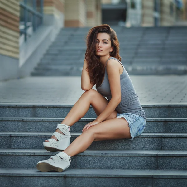 Retrato de estilo de vida al aire libre de una chica joven y bonita posando en la escalera, usando un estilo urbano hipster sobre fondo urbano . —  Fotos de Stock