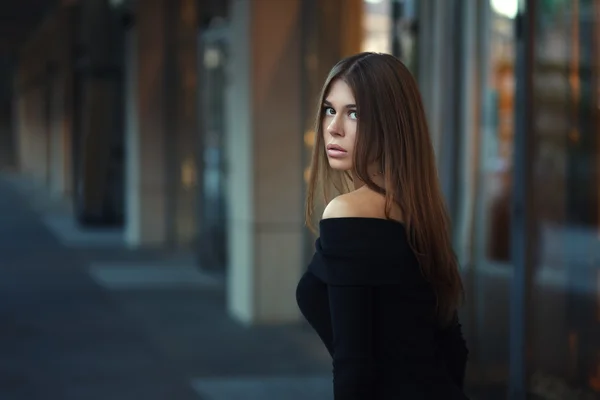 Mulher jovem morena bonita em vestido preto agradável. Posando sobre fundo urbano. Foto de moda — Fotografia de Stock