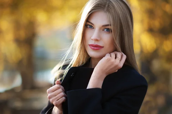 Mulher jovem loira bonita em casaco preto agradável. Posando sobre fundo de outono dourado. Foto de moda — Fotografia de Stock