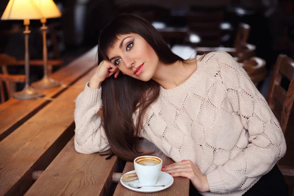 Close-up lifestyle portrait of pretty young woman in wool sweater drinking coffee and dreaming. Early morning in cafe, comfortable breakfast concept. — Stockfoto