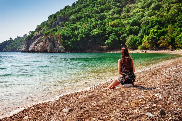 Portré, szép cserzett nő ül a tenger partján. Forró nyári napon, és ragyogó napsütéses fény. Panoráma-tenger partján, Kemer, Antalya, Törökország közelében. — Stock Fotó