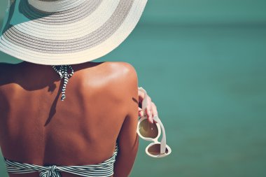 Seksi güzel birkadın çizgili bikini ve deniz arka plan üzerinde yaratıcı beyaz güneş gözlüğü ile şapka arkası.