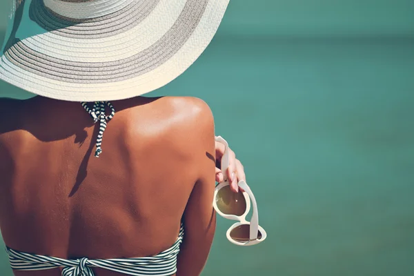 Seksi güzel birkadın çizgili bikini ve deniz arka plan üzerinde yaratıcı beyaz güneş gözlüğü ile şapka arkası. — Stok fotoğraf