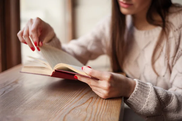 Ragazza che tiene in mano un libro indossato in caldo pullover di lana con smalto rosso gel manicure. Fondo in legno retrò. Studente donna concetto . — Foto Stock