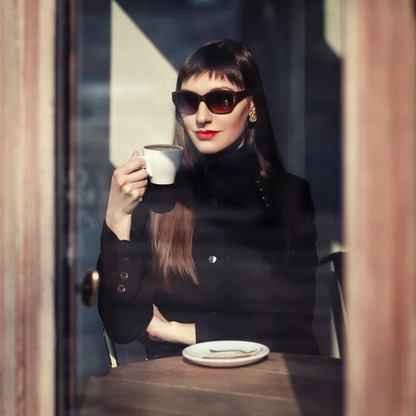 Jeune femme de mode assise dans un café dans la rue avec une tasse de cappuccino. Portrait extérieur dans un style rétro — Photo