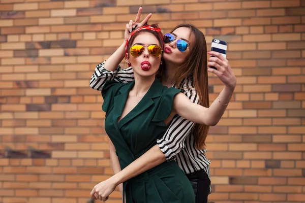 Deux jeunes femmes sexy posant pour selfie et riant avec tonque. Style de vie portrait sur fond de rue ville — Photo