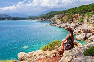 Turist kız oturan ve eski Yunan kasabası Phaselis koyda bakıyor. Kemer, Antalya, Türkiye yakınlarındaki sahilde panoramik manzara. 