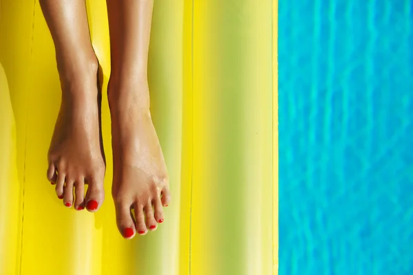 Porträt einer schönen, braun gebrannten Frau, die sich im Schwimmbad entspannt. gelbe aufblasbare Matratze. Beine dicht auf. kreative Gel-Politur rote Pediküre und Maniküre. Heißer Sommertag, helles, sonniges Licht. — Stockfoto