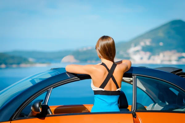 Piękna młoda kobieta z długimi włosami z powrotem z pomarańczowym Cabriolet na wybrzeżu Morza Śródziemnego — Zdjęcie stockowe