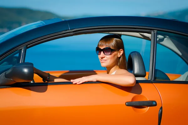 Beautiful young woman with long hair sitting in orange cabriolet at the Mediterranean sea coast — Stock Photo, Image