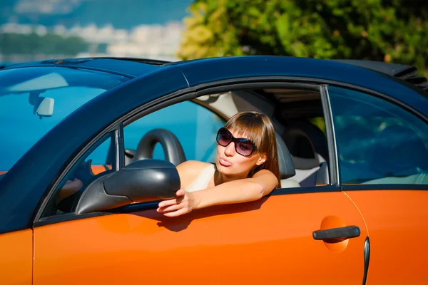 Beautiful young woman with long hair looking in mirror in orange cabriolet at the Mediterranean sea coast — Stock Photo, Image