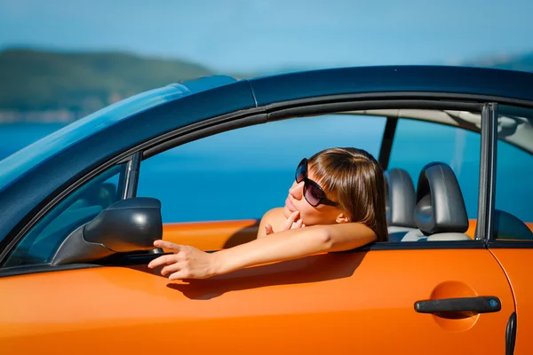 Beautiful young woman with long hair looking in mirror in orange cabriolet at the Mediterranean sea coast — Stock Photo, Image