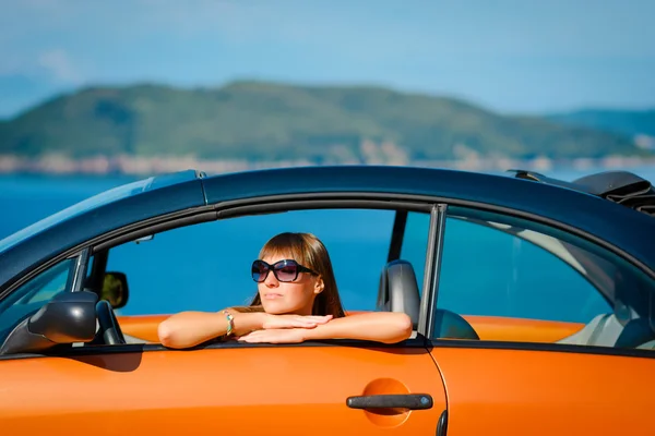 Beautiful young woman with long hair sitting in orange cabriolet at the Mediterranean sea coast — Stock Photo, Image