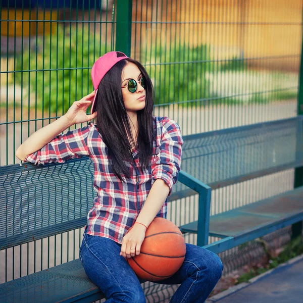 Estilo de vida ao ar livre retrato de muito jovem sentada menina, vestindo em estilo de grunge hipster swag com basquete em fundo urbano. Retro vintage tonificado imagem, simulação de filme . — Fotografia de Stock