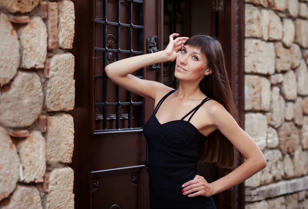 Retrato de estilo de vida al aire libre de una chica joven y bonita posando cerca de una vieja pared y puerta vintage, usando un vestido negro sobre fondo urbano. Creativo gel pulido manicura . —  Fotos de Stock