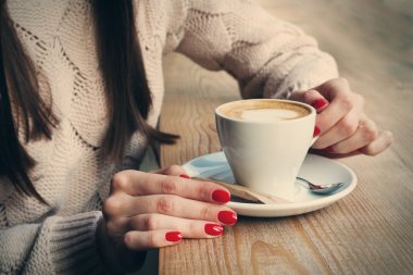 Fincan kahve kapuçino desen kalp ile köpük ile tutarak yakın çekim eller. Mükemmel kırmızı jel Lehçe manikür. Ahşap doğal masa. Yaratıcı renk sıcak mesaj işleme instagram tarzı.