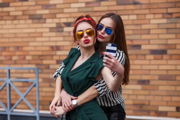 Deux jeunes femmes sexy posant pour selfie et riant avec tonque. Style de vie portrait sur fond de rue ville — Photo