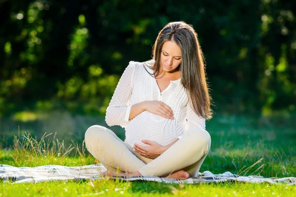 Mujer embarazada joven relajándose en el parque al aire libre, embarazo saludablec —  Fotos de Stock