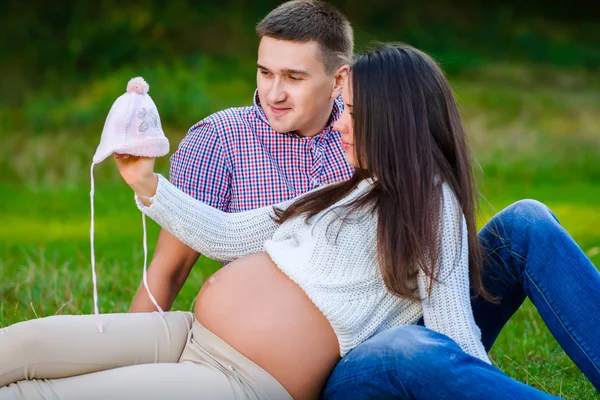 Glückliches und junges schwangeres Paar betrachtet Babysachen in der Natur — Stockfoto