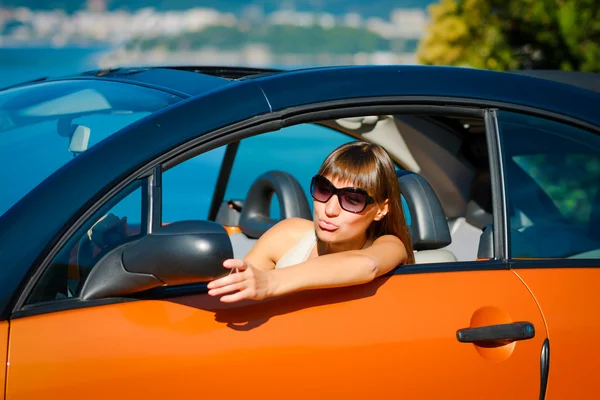 Beautiful young woman with long hair looking in mirror in orange cabriolet at the Mediterranean sea coast — Stock Photo, Image