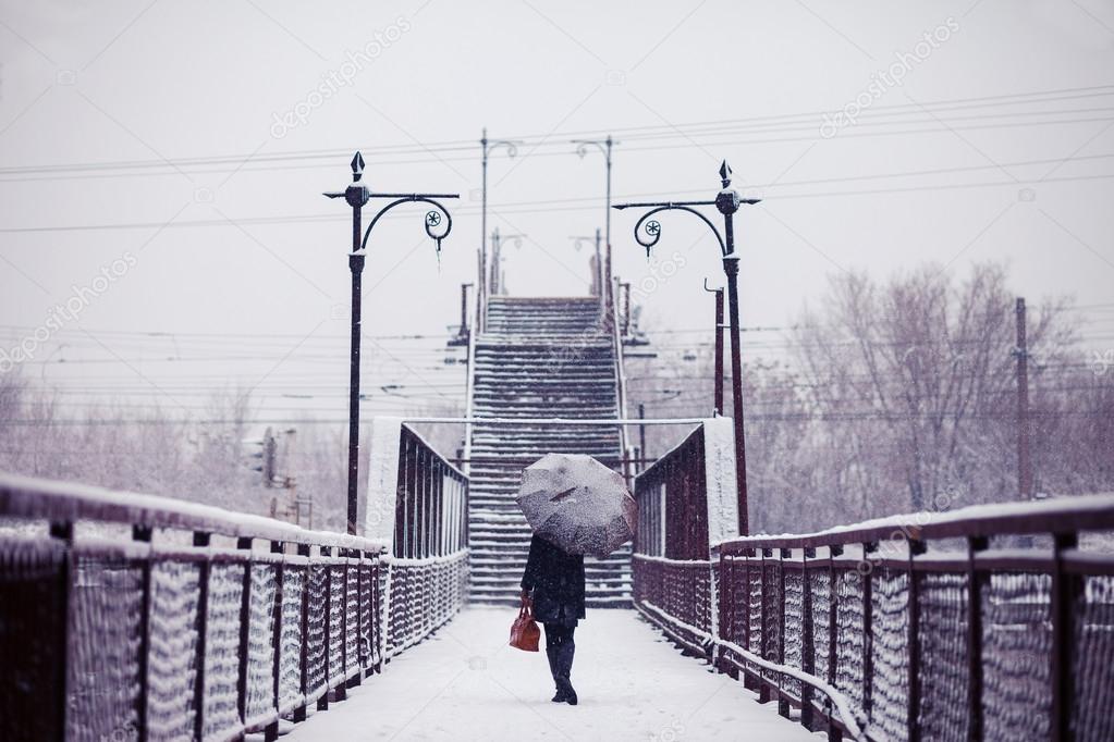 Young woman is going across the bridge in snowfall toned image