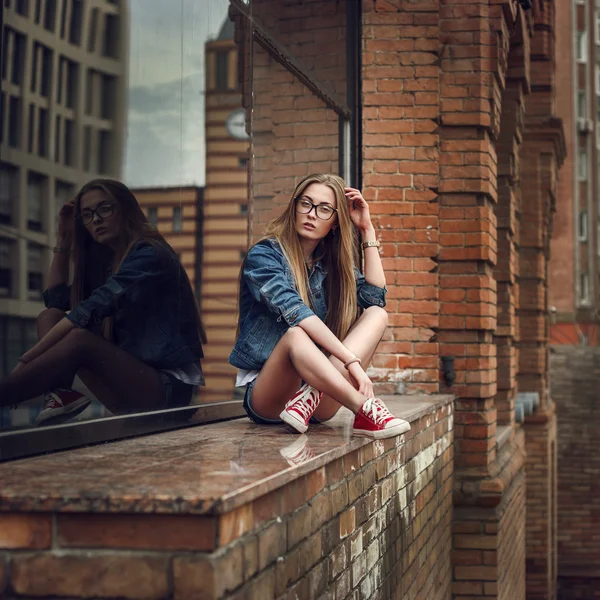 Outdoor-Lifestyle-Porträt eines hübschen jungen sitzenden Mädchens, das im Hipster-Swag-Grunge-Stil urbanen Hintergrund trägt. Retro Vintage getöntes Image, Filmsimulation. — Stockfoto