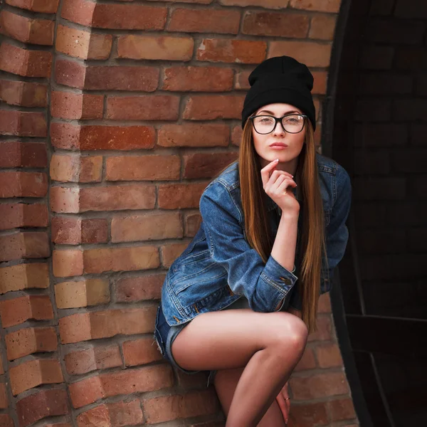 Jovem mulher hipster sexy vestindo jaqueta jeans, chapéu preto hipster e glasse. Estilo de vida retrato da cidade . — Fotografia de Stock