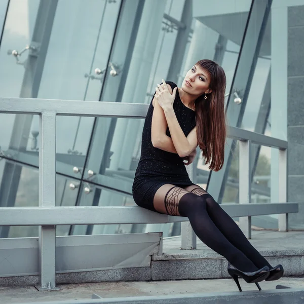 Retrato al aire libre de moda de mujer hermosa sexy con cabello castaño vistiendo en vestido negro, manguera y tacones altos. Posando sobre un fondo urbano creativo . — Foto de Stock