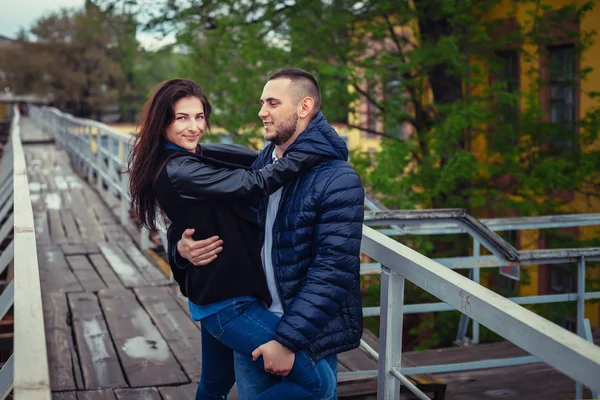 Beautiful young couple in love on a date outdoors on modern urban background. Smiling and hugging. Bearded handsome rustic man and brunette pretty woman in casual dress. — Stock Photo, Image