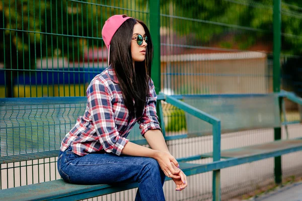 Jonge hipster stijl meisje buiten in creatieve zonnebril en cap. Stedelijke achtergrond — Stockfoto