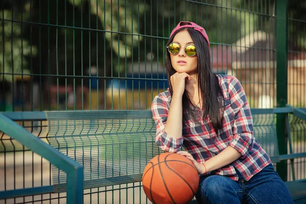 Buiten levensstijl portret van vrij jong meisje, dragen in hipster swag grunge stijl stedelijke achtergrond en creatieve zonnebril. Basketbal Hof en oranje bal. Retro vintage getinte afbeelding, film simula — Stockfoto