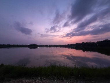 Gölün üzerinde güzel bir günbatımı. Suyun içinde gökyüzünün yansıması. Gökyüzü bulutlarla dolu. Huzurlu ve huzurlu bir atmosfer yaratıyor.