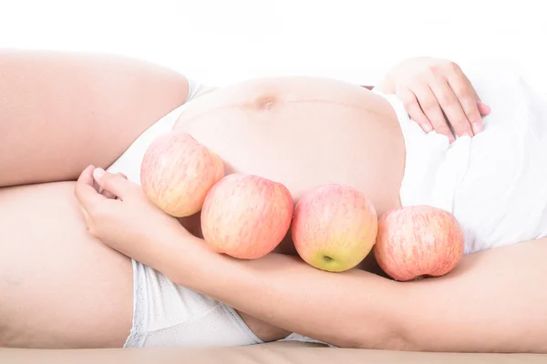 Mujer embarazada del vientre con manzanas alrededor y sostener una manzana — Foto de Stock