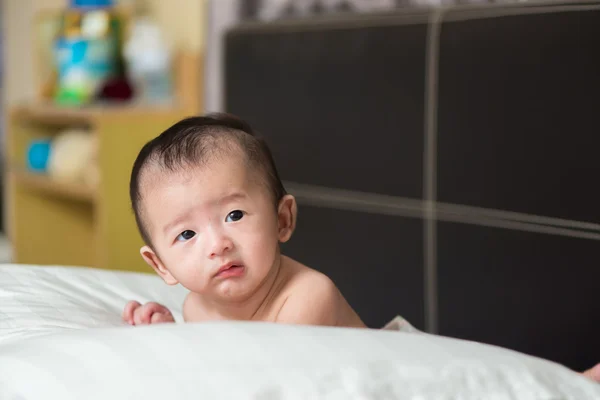 Infeliz bebê asiático bonito deitado em um travesseiro branco, na cama — Fotografia de Stock