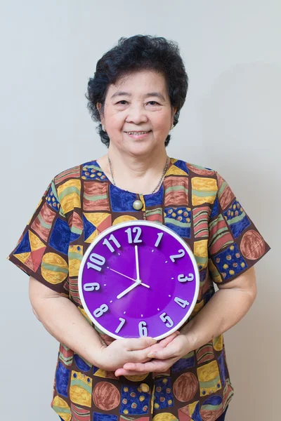 Asian senior woman holding purple clock in studio shot, specialt — Stock Photo, Image