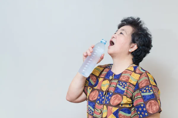 Asijské starší žena s láhev a sklenice vody, na červeno ye — Stock fotografie