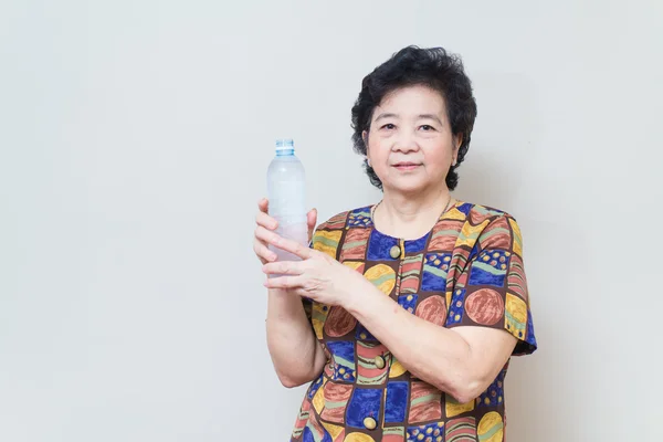 Asian senior woman with bottle and glass of water, on reddish ye — Stock Photo, Image