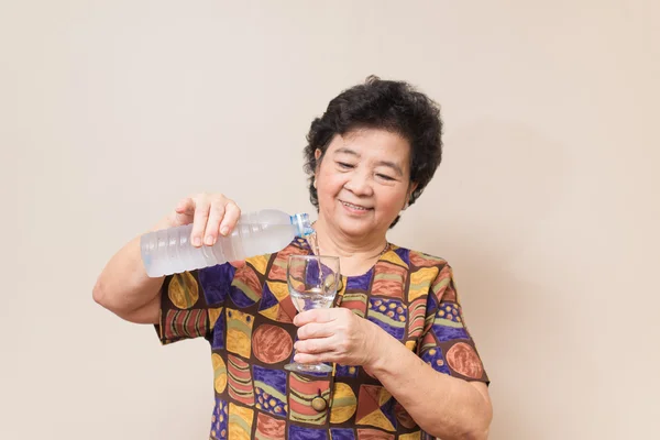 Asijské starší žena s láhev a sklenice vody, teplý tón — Stock fotografie