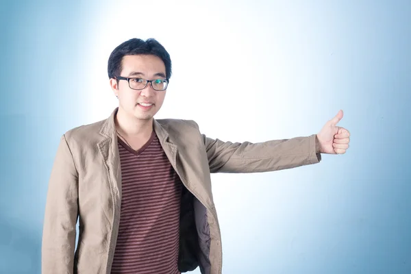 Азиатский парень делает большие пальцы вверх с улыбкой, на синем фоне — стоковое фото